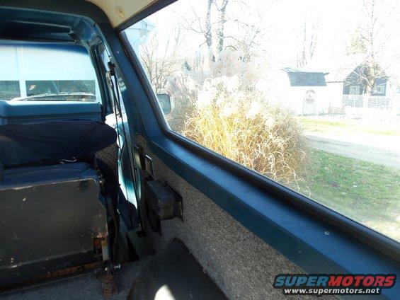 Interior view of a blue SUV, looking out the passenger window at dry grass and a house