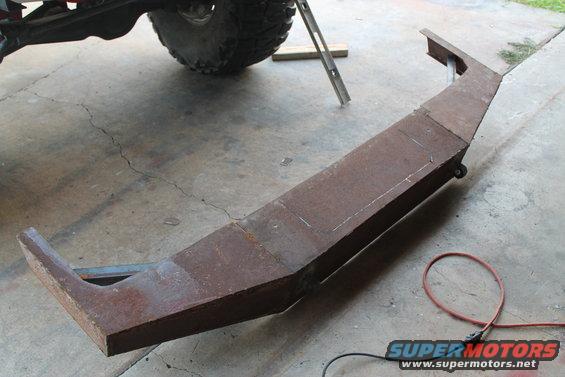 Custom fabricated steel bumper, rusty, with angled ends and a central section marked for cuts