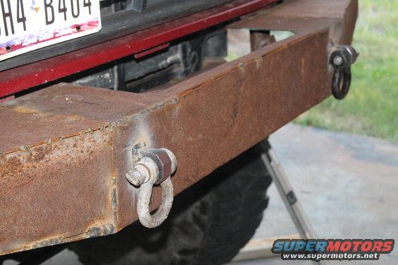 Rusty custom steel rear bumper with two D-ring tow hooks and a license plate