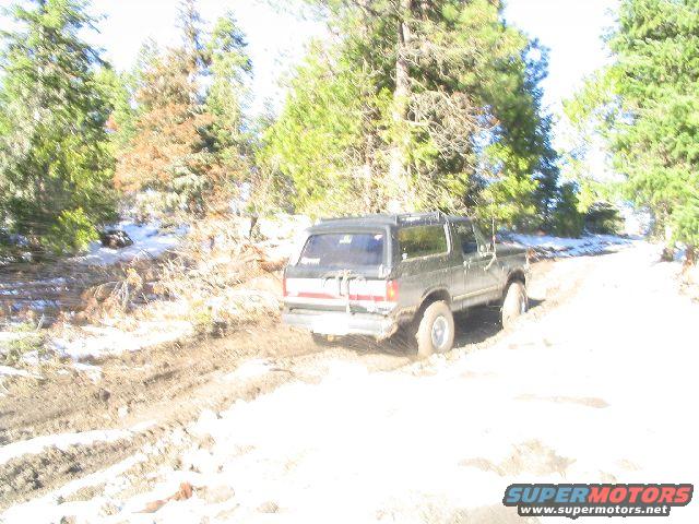 1987 Ford Bronco driving on a muddy, snowy dirt road through a forest