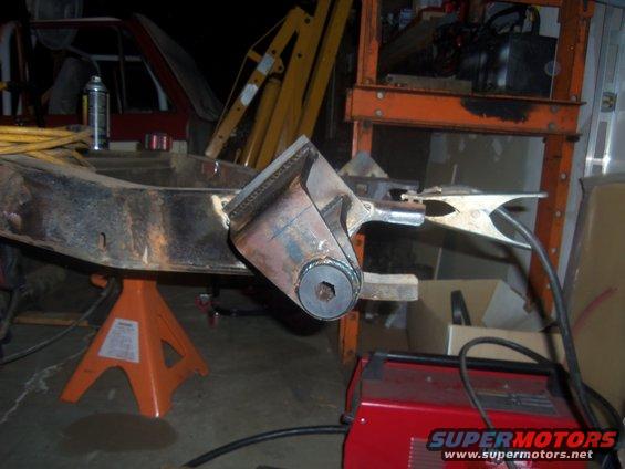 Welding equipment attached to a rusty vehicle frame supported by orange jack stands