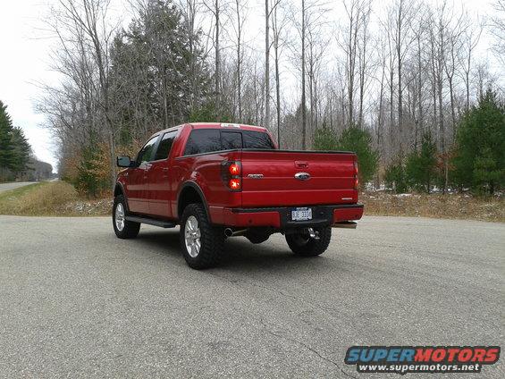 Red Ford F-150 pickup truck parked on a paved road with trees in the background