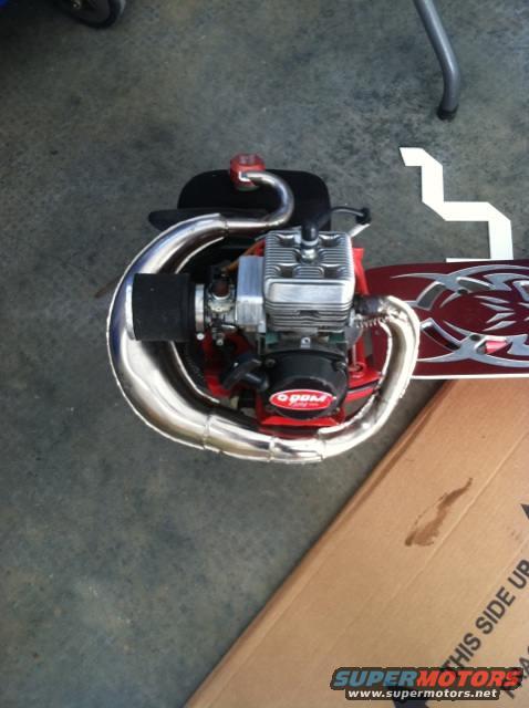 Motorized scooter engine with chrome exhaust pipe and red deck with tribal graphics