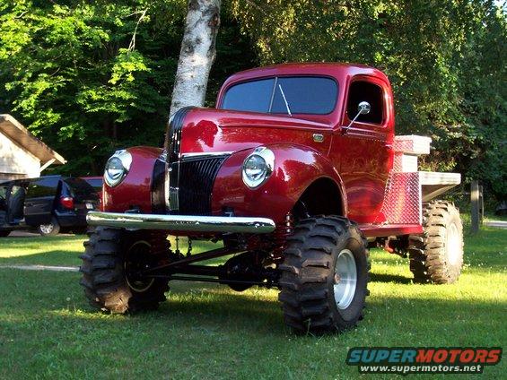 Red lifted pickup truck with big tires parked on grass, other vehicles in background