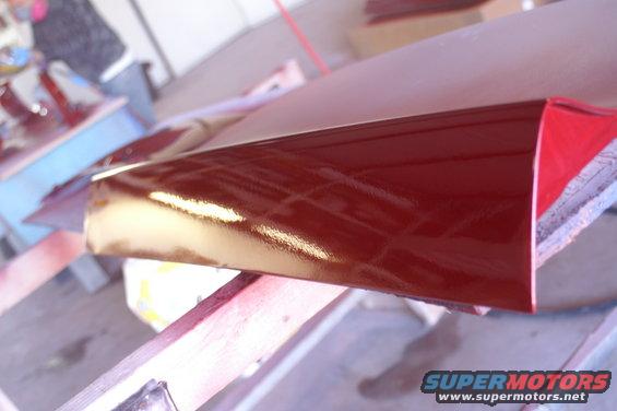Red car part with glossy finish, angled view, resting on wood