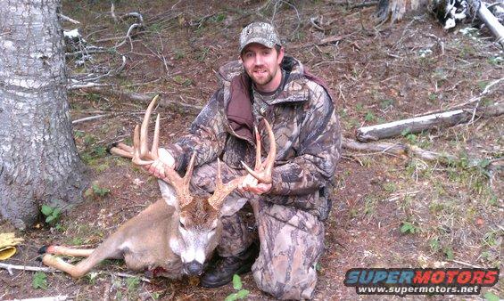 Man in camouflage kneeling with a large buck deer in a wooded area