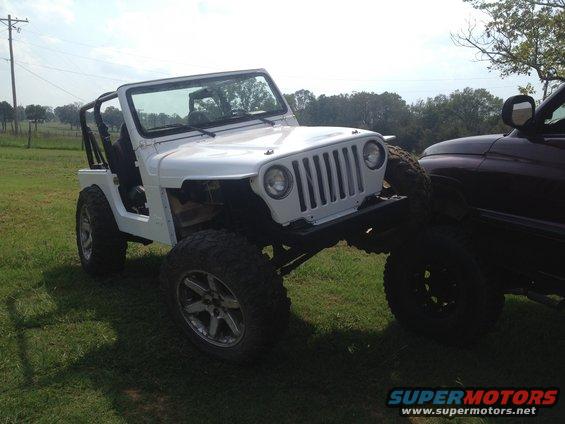 White Jeep Wrangler with aftermarket wheels and off-road tires, parked next to a dark-colored truck