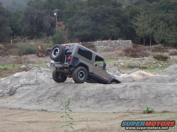Gray Jeep Wrangler with spare tire on rear, tilted on rocky terrain