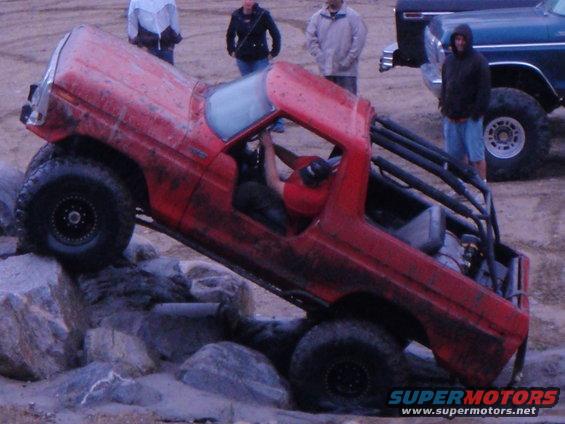 Red 1978 Ford Bronco with roll cage climbing over rocks