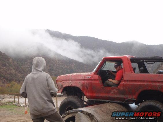 Red 1978 Ford Bronco side view, off-roading with a person in the driver's seat