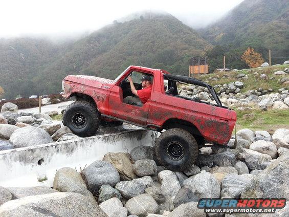 Red 1978 Ford Bronco off-roading over rocks