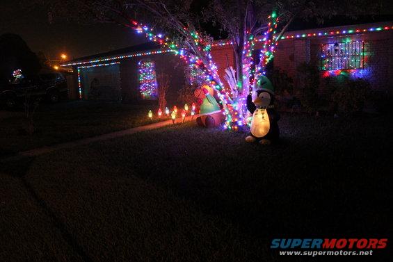 Dark scene of a house exterior at night, adorned with colorful Christmas lights and inflatable holiday figures on the lawn
