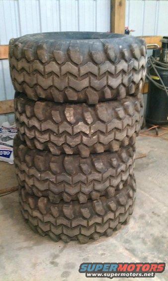 Stack of four large off-road tires with aggressive tread pattern