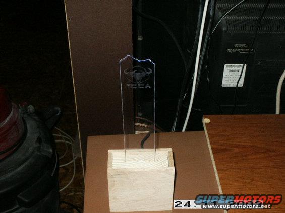 Acrylic trophy with bull logo and 'TECA' text on a wooden base, with electronics and furniture in the background