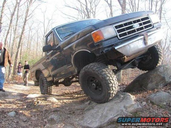 Black Ford pickup truck climbing over rocks on a trail. Driver is visible