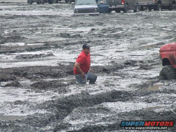 Red truck tire stuck in mud with a man kneeling nearby