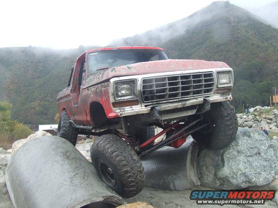 Red 1978 Ford Bronco with lifted suspension navigating rocky terrain