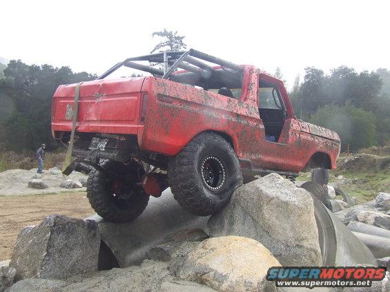 red off-road SUV with roll cage climbing over rocks