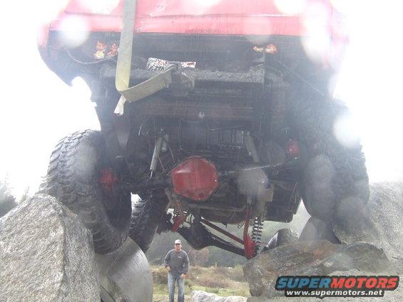 Red SUV with large tires stuck on rocks, viewed from underneath