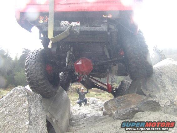 Rear view of a red off-road vehicle on rocks, with a person crouching below