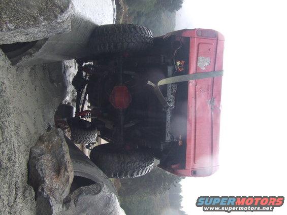 Red off-road vehicle on its side, stuck between large rocks. Undercarriage and rear tire are visible