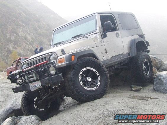 Tan Jeep Wrangler Rubicon with aftermarket bumper and winch on rocky terrain