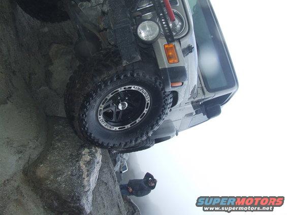 Jeep Wrangler tilted on rocks with a person below