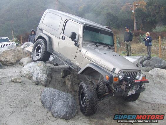 Silver Jeep Wrangler Rubicon off-roading over rocks, front right tire elevated