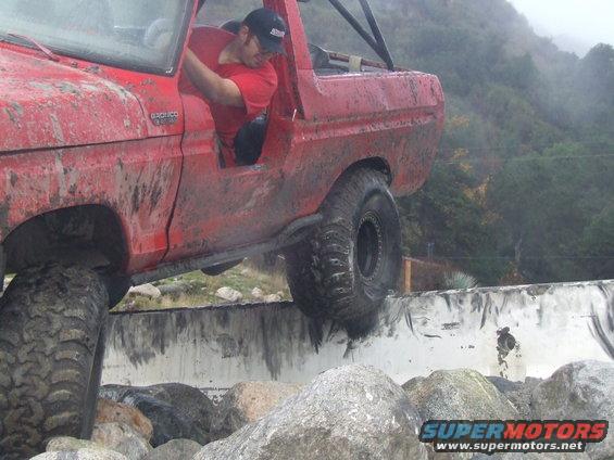 Red 1978 Ford Bronco climbing over rocks, driver visible