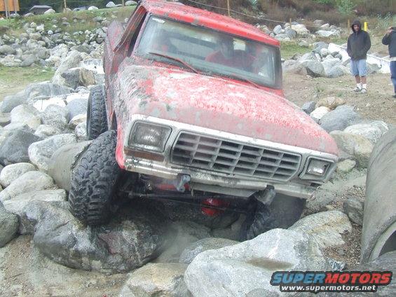 Red pickup truck with large tires navigating large rocks