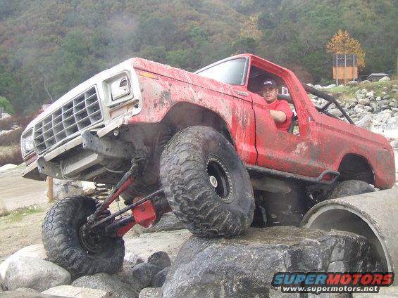Red 1978 Ford Bronco climbing rocks, front 3/4 view