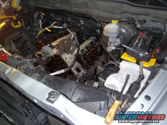 Engine bay of a 2002 Dodge 1500 with engine partially disassembled, showing the V8 engine block and various components. Tools are visible
