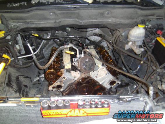 Engine bay with valve covers removed, showing internal components and tools on the workbench