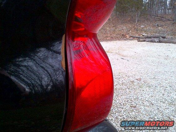 Close-up of a red tail light on a black vehicle. Some damage is visible near the seam