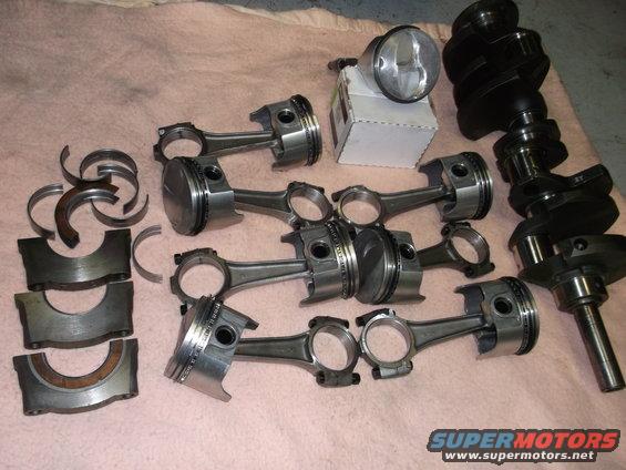 Engine parts including pistons, connecting rods, crankshafts, and bearings on a pink surface.