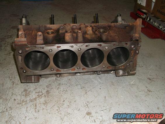 Engine block with four cylinders visible, resting on a concrete floor