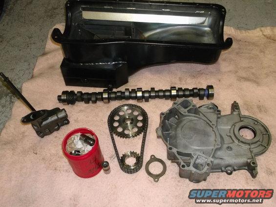 Engine parts laid out: black oil pan, camshaft, timing chain with gears, timing cover, oil pump, and lifters in a red container