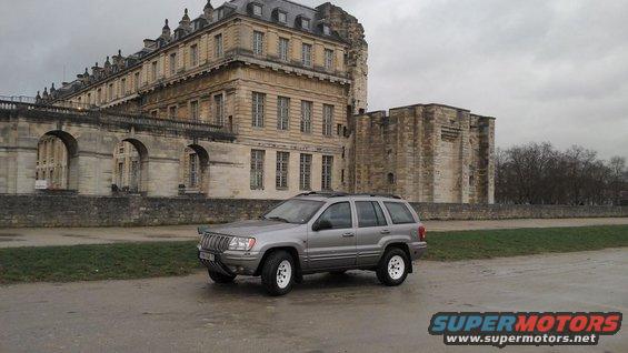 Silver Jeep Grand Cherokee with white wheels parked outside a chateau
