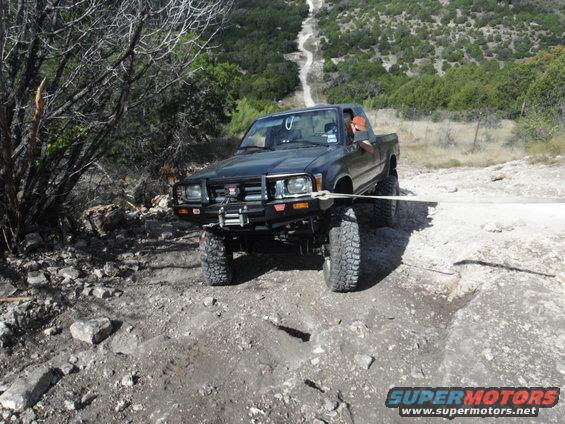 Black Toyota pickup truck with winch on front bumper, being pulled by a strap on a dirt road