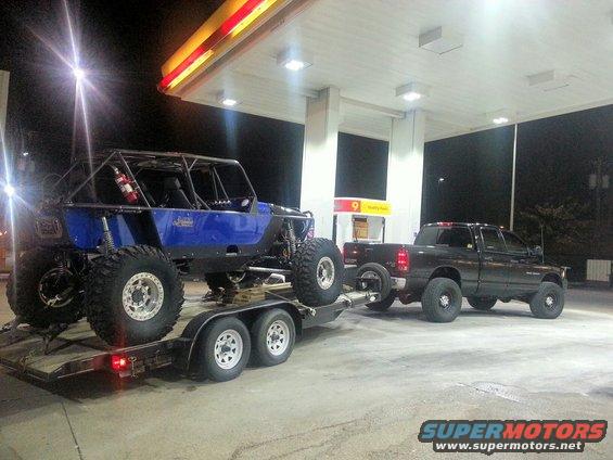Blue off-road buggy on trailer towed by pickup truck at gas station