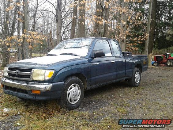 Blue Toyota Tacoma pickup truck parked outside with snow on the hood and trees in the background