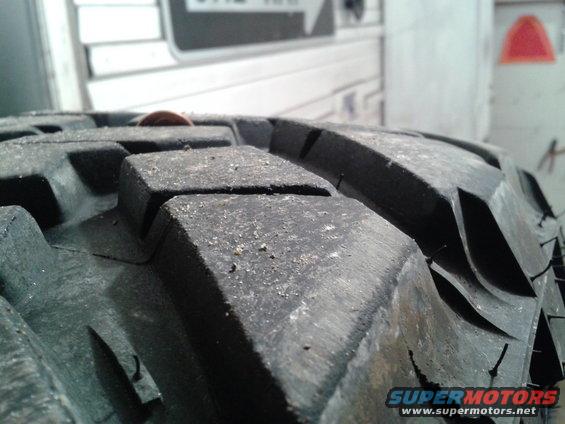 Close-up of a large, knobby tire tread with a penny on top