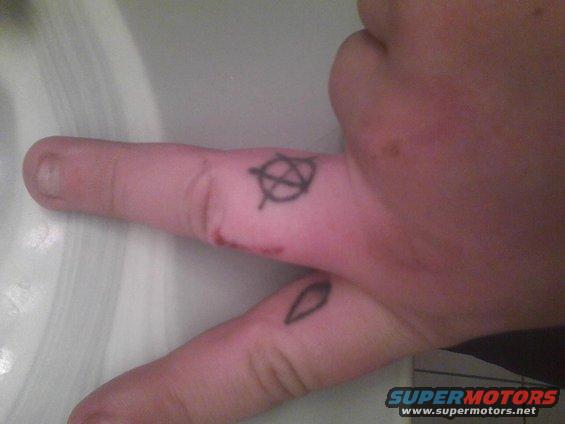Hand showing peace sign with anarchy symbol and leaf tattoos on fingers