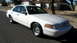 2001 Ford Crown Victoria - A white 2001 Ford Crown Victoria is parked on the side of a street in front of a house.