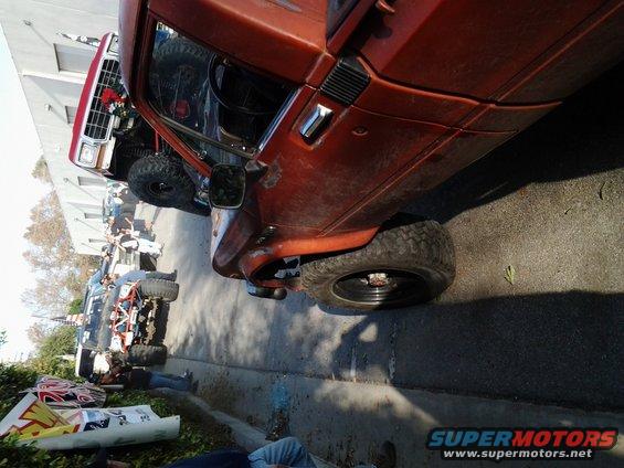 Several modified off-road vehicles parked on a street, including a red pickup truck and a rusty orange SUV