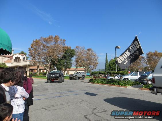 Several modified SUVs and trucks parked on asphalt with a building and trees in the background