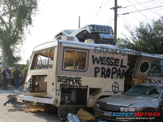 Camper van with a car on its roof, graffiti on the side, and a sedan parked next to it