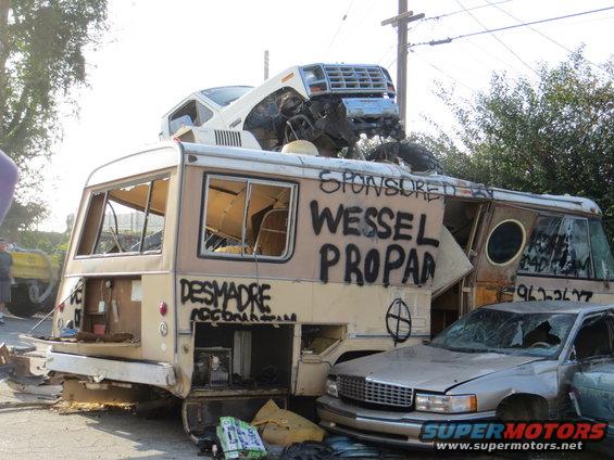 Wrecked RV with a car on top, graffiti on side