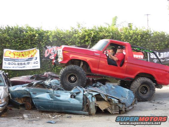Red 1978 Ford Bronco with lifted suspension crushing two wrecked cars