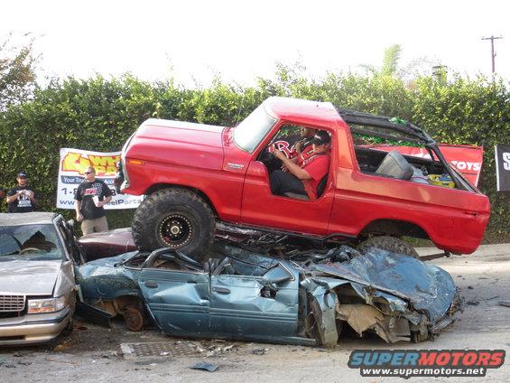 Red 1978 Ford Bronco crushing a blue sedan, 3q-front view